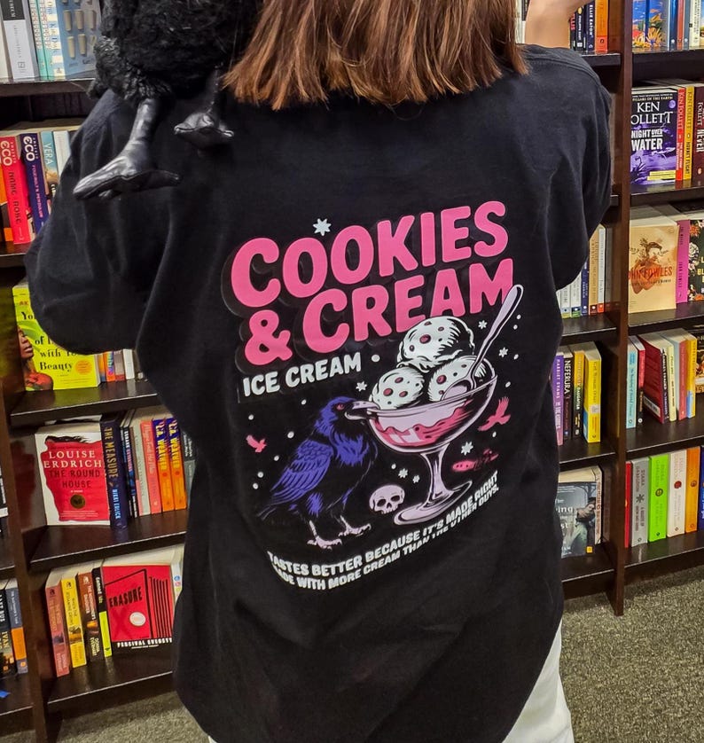 Puede incluir: Camiseta negra con un gr&aacute;fico rosa y blanco que dice "Cookies & Cream Ice Cream". El dise&ntilde;o incluye un cuervo, un helado y el texto "Tastes better because it's made right with more cream than the".