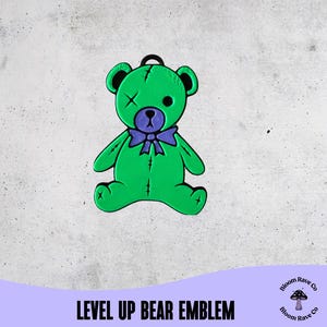 Puede incluir: Un emblema de oso verde con una pajarita morada y un parche en el ojo negro. El oso tiene orejas negras y un lazo negro en la parte superior. El texto "LEVEL UP BEAR EMBLEM" está en la parte inferior.
