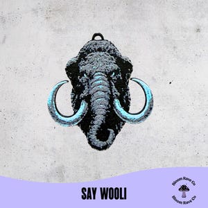 May include: A black mammoth pendant with blue accents on the tusks and eyes. The pendant has a textured surface and a loop at the top for hanging. The text "SAY WOOLI" is at the bottom.