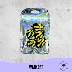 May include: A clear, iridescent bag containing five black and yellow charms. Each charm has the word "WANKDAT" printed on it. The bag is sealed and has a small hole at the top. The word "WANKDAT" is also printed in large, black letters at the bottom.