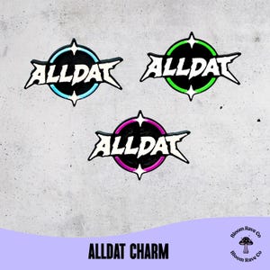 May include: Three circular enamel pins featuring the text ALLDAT in a jagged white font. Each pin has a black centre and a coloured outer ring in light blue, neon green, or bright pink, with four-pointed star accents at the top and bottom.