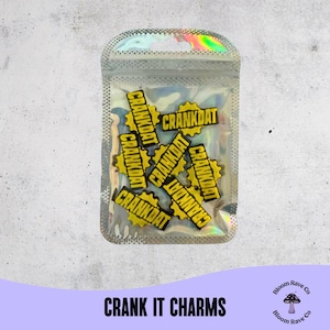 Puede incluir: Una bolsa transparente e iridiscente que contiene múltiples amuletos amarillos y negros "CRANKDAT". Los amuletos tienen forma de engranajes. El texto "CRANK IT CHARMS" está en la parte inferior de la imagen, con un logotipo de hongo.