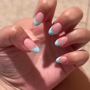 Op de afbeelding: Een set amandelvormige vingernagels in een klassieke French manicurestijl met een glanzende, nude-kleurige basis en levendige, lichtblauwe uiteinden. De nagels zijn netjes verzorgd en vertonen een gladde, gepolijste afwerking op alle vijf vingers.