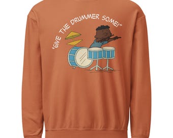 May include: A rust-colored sweatshirt with a cartoon illustration of a drummer playing a drum set. The illustration includes a blue drum set and the text "GIVE THE DRUMMER SOME!" in a curved white font.