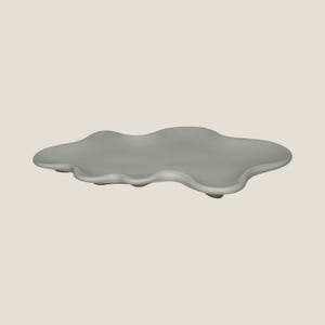 May include: A pale grey ceramic serving tray in the shape of a cloud. The tray features a wavy edge and is supported by three small, rounded feet. Its neutral colour and organic form suit various home decor schemes.