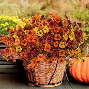 May include: A woven basket overflowing with colorful autumn flowers in shades of orange, yellow, and burgundy. The basket is set against a blurred background, with a pumpkin visible on the right.