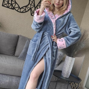 May include: A blue hooded robe with pink trim and elephant pattern. The robe has a belt and pockets. A black metal LOVE sign is on the wall behind the robe.