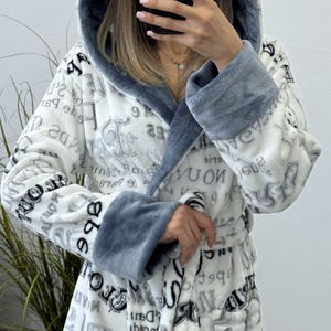 May include: A white hooded robe with a gray trim and a matching belt. The robe is covered in a repeating pattern of gray text and numbers. The cuffs and hood lining are a solid gray color.