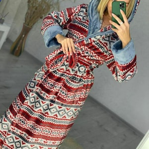 May include: A long, hooded robe with a geometric pattern in red, white, and gray. The robe has a soft, plush texture and features light blue trim on the hood and cuffs. A matching belt is tied around the waist.