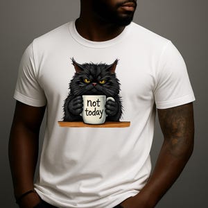 Op de afbeelding: Wit T-shirt met een chagrijnige zwarte kat die een mok vasthoudt met de tekst "not today". De kat heeft gele ogen en zit op een houten plank. Het T-shirt heeft een ronde hals.