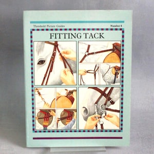 May include: A light blue book titled "FITTING TACK" with illustrations demonstrating the process. The book has a teal border with a maroon and white dotted design. The cover features a horse's head and hands adjusting the tack.