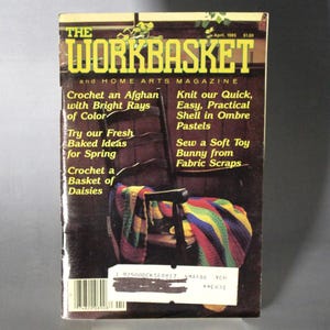 May include: The Workbasket magazine cover from April 1985 features a colourful crocheted afghan draped over a wooden chair. The cover text includes "Crochet an Afghan with Bright Rays of Color", "Knit our Quick, Easy, Practical Shell in Ombre Pastels", "Try our Fresh Baked Ideas for Spring", "Crochet a Basket of Daisies", and "Sew a Soft Toy Bunny from Fabric Scraps".