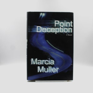 Puede incluir: Portada de libro con fondo negro y un camino azul y amarillo serpenteando por el centro. El título "Point Deception" está en texto blanco con el subtítulo "Una novela" en texto blanco más pequeño. El nombre del autor "Marcia Muller" está en texto blanco en la parte inferior de la portada.