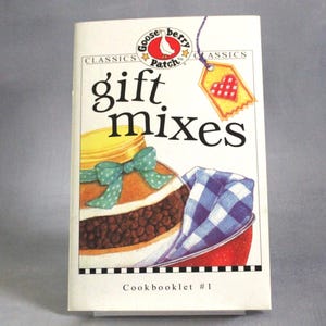 May include: A cookbook titled "Gift Mixes" by Gooseberry Patch. The cover shows a jar with a green bow, a red bowl with a blue and white checked cloth, and a tag with a heart. The cookbook is labelled "Classics" and "Cookbooklet #1".