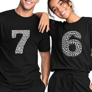 Könnte beinhalten: Zwei Personen tragen schwarze T-Shirts. Eines hat eine große weiße Zahl 7, die aus kleineren 6en besteht. Das andere hat eine große weiße Zahl 6, die aus kleineren 7en besteht. Beide lächeln.