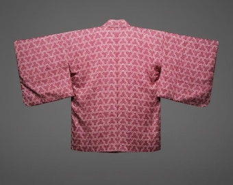 Puede incluir: Un kimono rosa con un patrón geométrico repetitivo en un tono más claro de rosa. El kimono tiene mangas anchas y un cuello. La prenda se muestra sobre un fondo gris.
