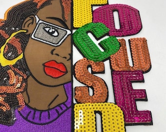 May include: Embroidered patch featuring a woman's face with sunglasses and the word "FOCUSED" in sequined letters. The woman has brown skin, red lips, and a purple sweater. The letters are yellow, green, orange, and pink.