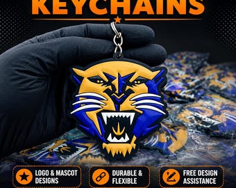 May include: A custom PVC keychain featuring a stylized yellow and blue panther head mascot with white teeth and whiskers, attached to a metal split ring. The text CUSTOM PVC KEYCHAINS is displayed above, with additional text below.
