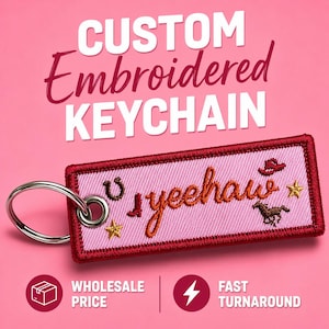 May include: Custom embroidered keychain with a pink background and red border. The keychain features the word "yeehaw" in orange embroidery, along with a horseshoe, cowboy hat, stars, and a horse. The text "Custom Embroidered KEYCHAIN" is at the top.