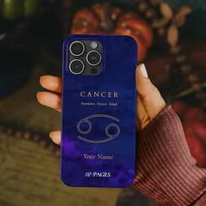 Puede incluir: Funda de teléfono azul marino con el signo zodiacal de Cáncer. La funda tiene la palabra "CANCER" en letras doradas, junto con los rasgos "Sensitive, Fierce, Kind". El diseño incluye un símbolo de Cáncer dorado y espacio para un nombre, con el texto "12-PAGES".