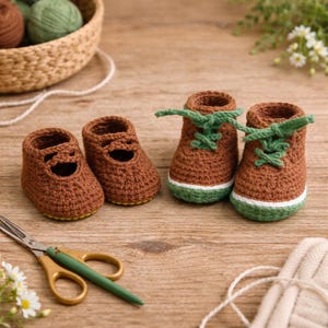 Op de afbeelding: Handgemaakte gehaakte babyschoenen in bruin met groene en witte accenten. Er zijn twee paar schoenen te zien: een paar Mary Janes en een paar sneakers met groene veters. De schoenen liggen op een houten oppervlak.