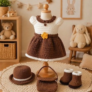 Può includere: Un completo all'uncinetto fatto a mano per bambini, con un vestito bianco e marrone con una stella, un cappello, una borsa e stivali abbinati. L'abito è esposto su un manichino. Il set è realizzato con filato marrone e bianco.