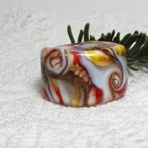 May include: A white, red, brown, and yellow glass ring with a swirling pattern.