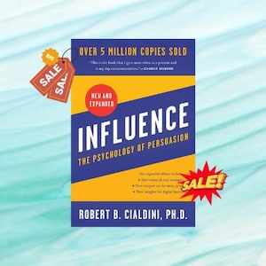 Könnte beinhalten: Ein Buch mit dem Titel "Influence: The Psychology of Persuasion" mit einem blauen, gelben und weißen Einband. Der Einband enthält den Namen des Autors, Robert B. Cialdini, Ph.D., und den Text "Über 5 Millionen Exemplare verkauft". Verkaufs-Tags sind ebenfalls sichtbar.