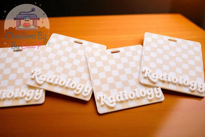 May include: Several cream-colored badge holders with a checkered pattern and the word "Radiology" in a 3D font. Each badge has a slot for a lanyard. The badges are arranged on a wooden surface.
