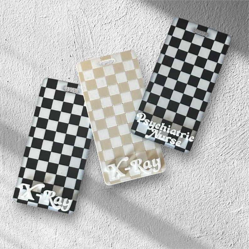 May include: Three rectangular badge holders with a checkered pattern. One is black and white, one is beige and white, and the third is black and white with the text "Psychiatric Nurse". The bottom of two badge holders have the text "X-Ray".