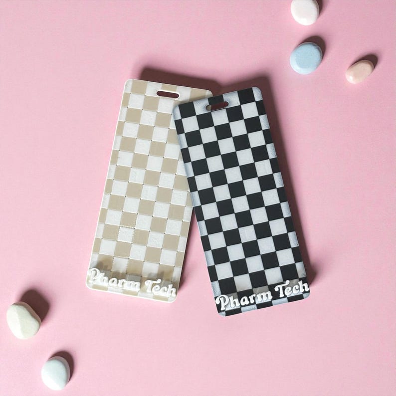 May include: Two rectangular phone cases with a checkered pattern. One case is beige and the other is black and white. The text "Pharm Tech" is printed on the bottom of each case. The cases are on a pink background.