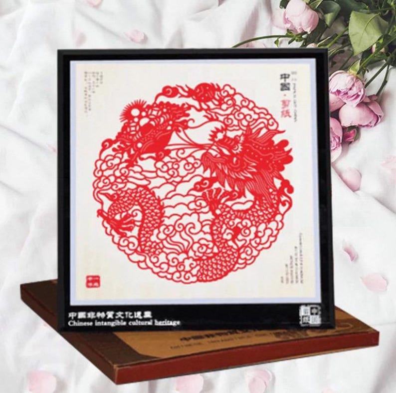 May include: Framed red paper cut art featuring a detailed dragon design within a circular frame. The artwork is set against a white background and framed in black. The text "Chinese intangible cultural heritage" is visible.