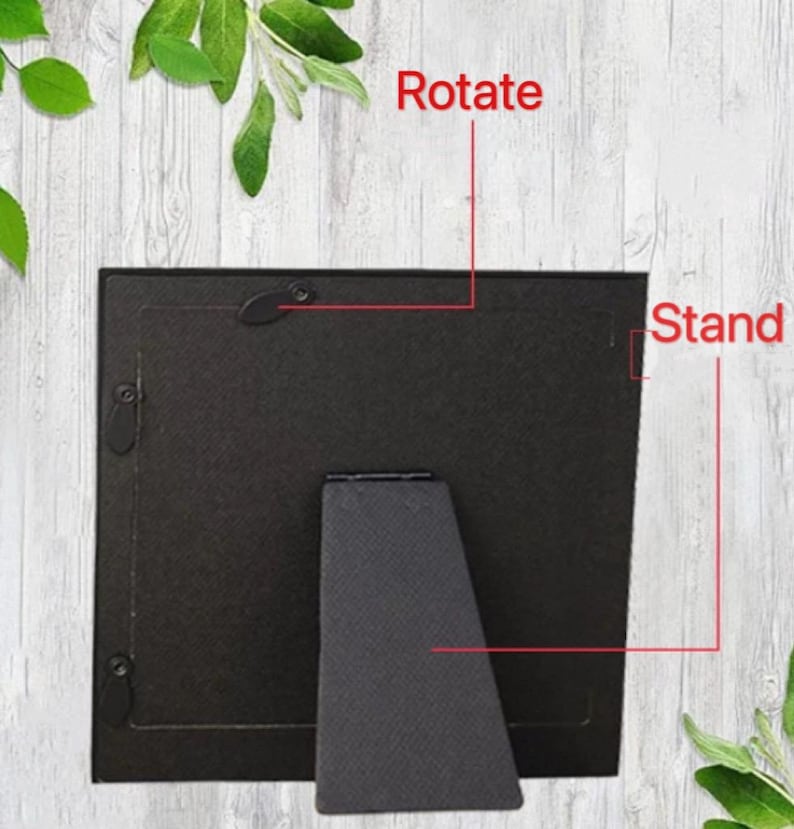 May include: A black picture frame with a stand and a rotating mechanism. The word "Rotate" is written above the frame, and the word "Stand" is written to the right. The frame is set against a light wood-grain background.
