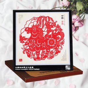 May include: A framed red paper cut-out of a horse and monkey, a traditional Chinese art form. The artwork is set against a white background and framed in black. The text "Chinese intangible cultural heritage" is visible.