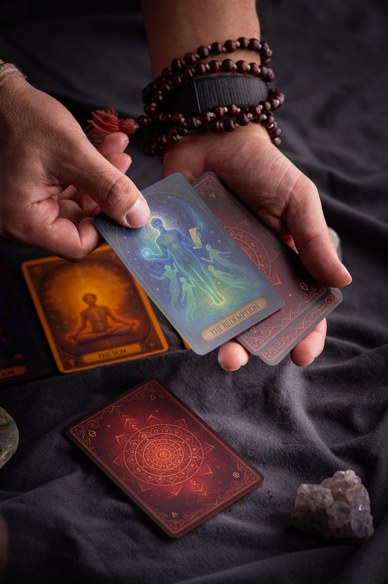 Pu&ograve; includere: Un mazzo di tarocchi con illustrazioni mistiche. Una carta, etichettata "THE REDEMPTION", presenta una figura con esseri eterei. Altre carte mostrano una figura che medita e un disegno circolare. Le carte sono tenute su uno sfondo grigio scuro.