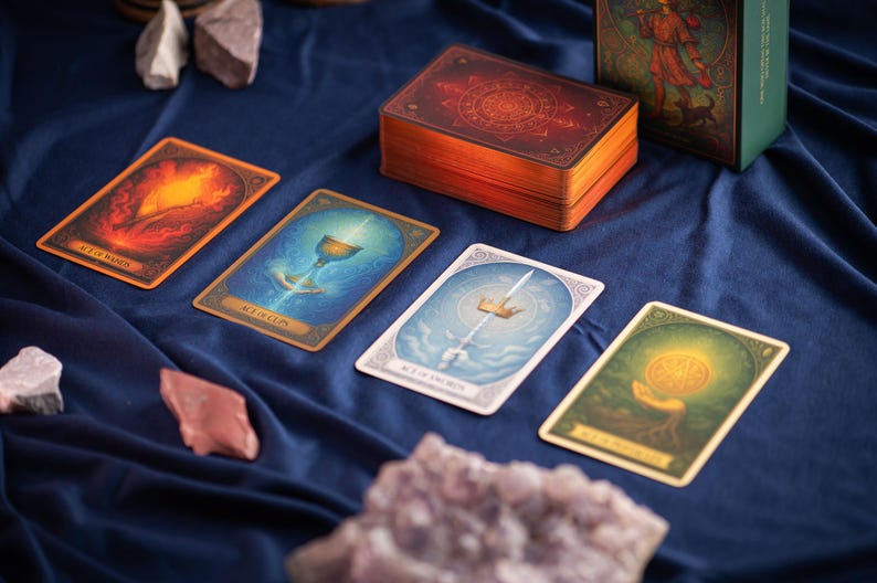 Pu&ograve; includere: Un mazzo di carte dei tarocchi con quattro carte esposte, con illustrazioni colorate e dettagli dorati. La scatola del mazzo &egrave; rosso scuro con disegni dorati. Le carte sono disposte su un tessuto blu scuro, con cristalli in primo piano.