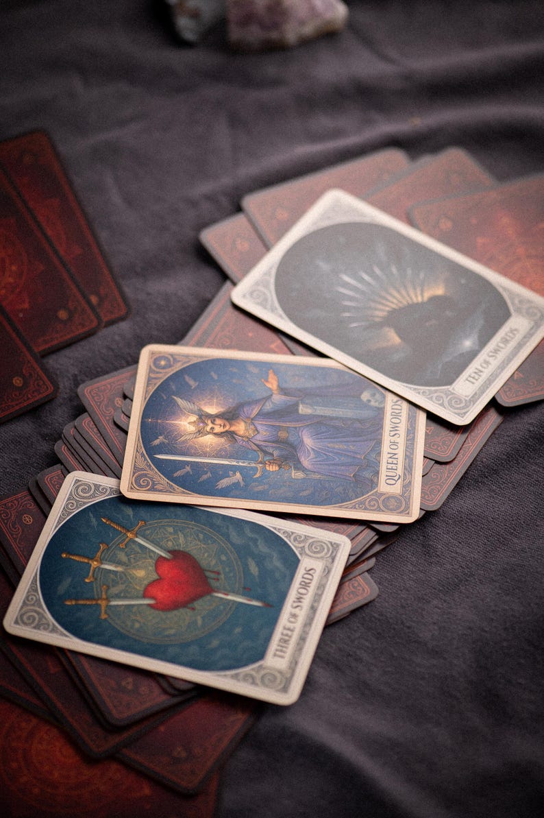 Pu&ograve; includere: Un mazzo di carte dei tarocchi con illustrazioni dettagliate. Le carte presentano immagini di una regina, spade e un cuore trafitto da spade. Le carte sono su una superficie scura, con altre carte visibili sullo sfondo.