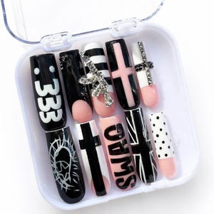 Puede incluir: Un conjunto de diez uñas postizas en una caja de plástico transparente. Las uñas presentan varios diseños, incluyendo el número "333", rayas, cruces y la palabra "SWAG". Los colores incluyen negro, blanco, rosa y plateado.