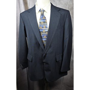 Peut inclure: Un blazer à fines rayures bleu marine avec une chemise blanche et une cravate à motifs. Le blazer a deux poches avant et une fermeture à deux boutons. La cravate présente un motif bleu et beige.