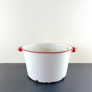 Pode incluir: Tigela de esmalte branco com borda vermelha e duas alças. A tigela tem um visual vintage com algum desgaste.