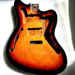 May include: A hollow-body electric guitar body with a sunburst finish. The body is made of wood and features a black edge, orange and red gradient, and a natural wood grain center. It has cutouts for the pickups, bridge, and f-holes.