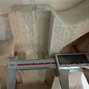May include: A digital caliper measuring the width of a wooden object. The caliper displays a measurement of approximately 1.25 inches. The wood has a light brown color and visible grain.