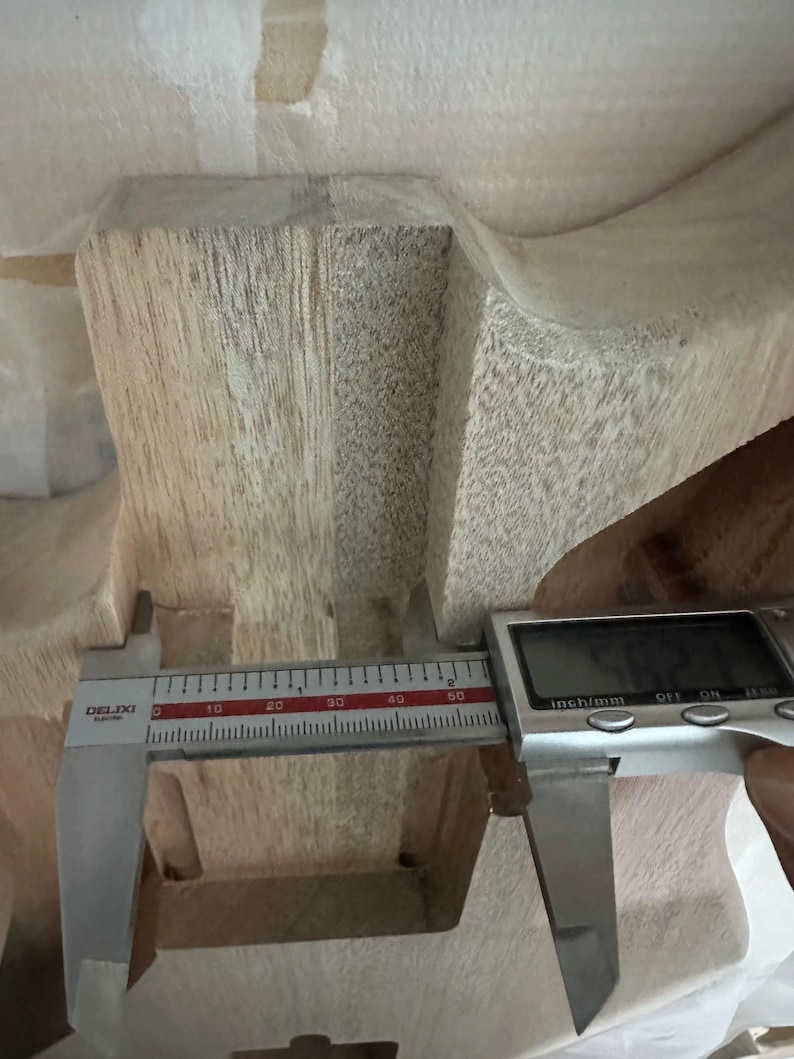 May include: A digital caliper measuring the width of a wooden object. The caliper displays a measurement of approximately 1.25 inches. The wood has a light brown color and visible grain.