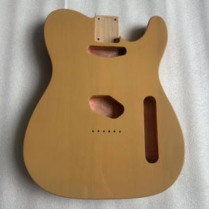 Puede incluir: Cuerpo de guitarra marr&oacute;n claro con recortes para pastillas, controles y m&aacute;stil. El cuerpo tiene un acabado liso y est&aacute; listo para el montaje. La veta de la madera es visible y el cuerpo est&aacute; dise&ntilde;ado para una guitarra estilo Telecaster.