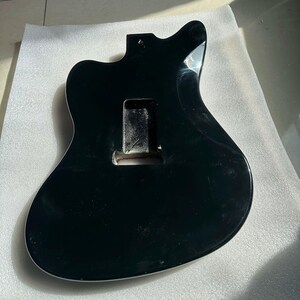 May include: A black guitar body with a white trim. The body has a cutaway design and a rectangular cavity for the electronics. The surface is glossy and reflects light. The guitar body is likely for a solid-body electric guitar.
