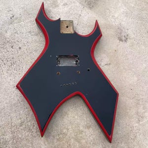 Guitarra con una sola pastilla humbucker, cuerpo negro estilo Warlock con ribete rojo, puente con cuerdas a través del cuerpo.