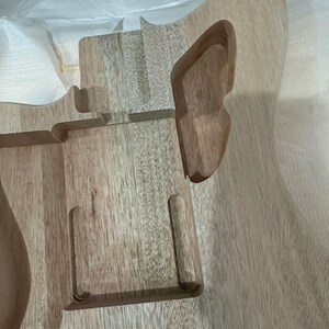 May include: Unfinished wooden guitar body with routed sections for components. The wood grain is visible, showing a light brown color. The body has a curved shape with cutouts for the neck and other hardware.