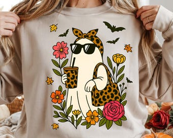 May include: Beige sweatshirt featuring a cartoon ghost wearing sunglasses and a leopard print headband. The ghost is holding a drink and a purse, surrounded by flowers and bats. The text "DIGITAL PNG FILE" is at the bottom.