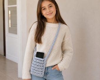 May include: A light blue crochet crossbody bag featuring a rectangular open-weave pattern and a single strap. The bag is constructed from yarn and includes a small white button closure at the top centre, designed to hold a smartphone securely.