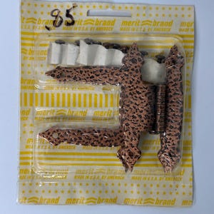 May include: A copper-colored metal strap hinge with a textured finish, packaged in a clear plastic blister pack on a yellow and white Merit Brand card. The card features the text Merit Brand Made in U.S.A. by Amerock and the handwritten number 85.